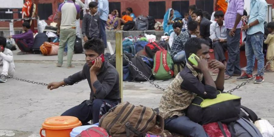 Indische Wanderarbeiter sitzen telefonierend auf ihrem Gepäck, während sie sich darauf vorbereiten, die Region Jammu und Kaschmir zu verlassen. Foto: Channi Anand/AP
