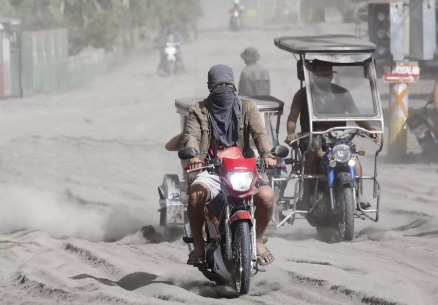 Einwohner fahren durch die Strassen voller Asche.