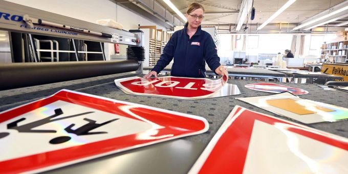 Bei der Firma Kurt Ries GmbH Schilderfabrik klebt eine Mitarbeiterin auf einen Blechrohling eine Folie, die mit einem Stop Verkehrsschild bedruckt ist. Bei der Firma Kurt Ries GmbH Schilderfabrik klebt eine Mitarbeiterin auf einen Blechrohling eine Folie, die mit einem Stop Verkehrsschild bedruckt ist.