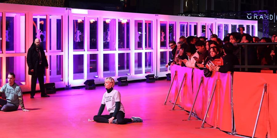 Zwei junge Menschen haben sich auf dem roten Teppich festgeklebt während der Eröffnung der Berlinale. Foto: Jörg Carstensen/dpa