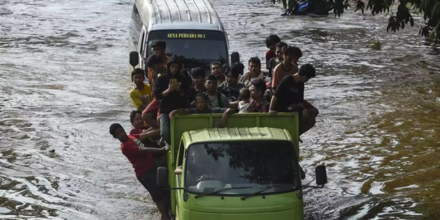 Menschen stehen auf der Ladefläche eines Transporters, um eine überflutete Strasse in Jakarta zu passieren. Foto: Agung Kuncahya B./XinHua/dpa