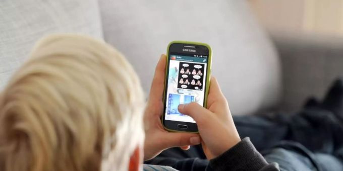 Ein Kind liegt auf einem Sofa und blickt auf sein Smartphone. Foto: Tobias Hase/dpa smartphone