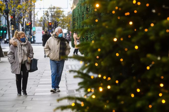 Menschen mit Mund-Nasen-Schutz gehen durch die weihnachtlich beleuchtete Oxford Street. Coronavirus - Grossbritannien
