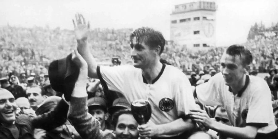 Der deutsche Stürmer und Kapitän Fritz Walter (M, oben) und sein Lauterer Teamgefährte Horst Eckel (r) werden nach dem Triumph im Fussball-WM-Finale im Berner Wankdorfstadion von begeisterten Anhängern vom Spielfeld getragen. Foto: picture alliance/dpa/Archivbild