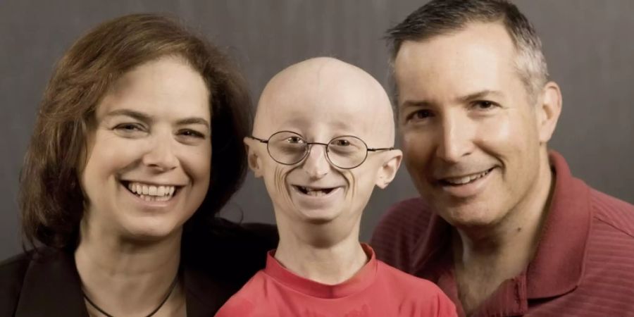 Der mit Progeria geborene Sam Berns zusammen mit seinen Eltern Leslie Gordon (l) und Scott Berns (r). Sam starb 2014 mit 17 Jahren. Seine Mutter gründete eine Progeria-Stiftung und ist Mitautorin einer aktuellen Studie, in der ein Heilverfahren erfolgreich an Mäusen getestet wurde. (Archivbild).