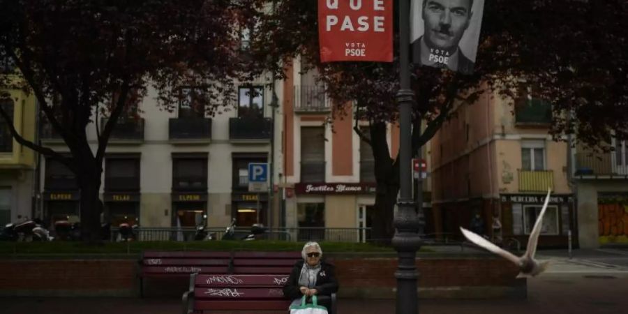 Eine Frau sitz auf einer Bank neben einem Wahlbanner für Sanchez, der spanische Ministerpräsident, mit dem Satz, «Mach es möglich». Sanchez liegt zwar in Umfragen seit Wochen mit rund 30 Prozent vorne. Foto: Alvaro Barrientos