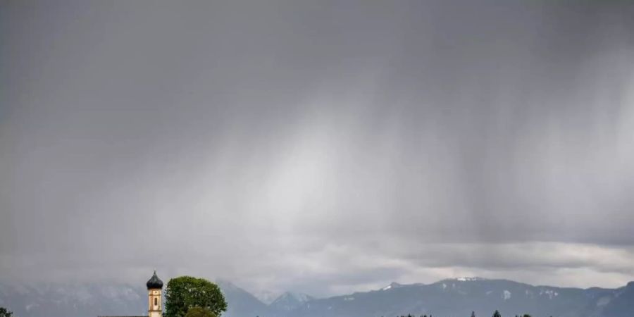 Dunkle Regenwolken ziehen über die Kirche St. Johannes der Täufer im bayrischen Rainsting. Foto: Sina Schuldt