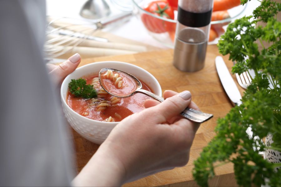 Person isst Tomatensuppe mit Nudeln