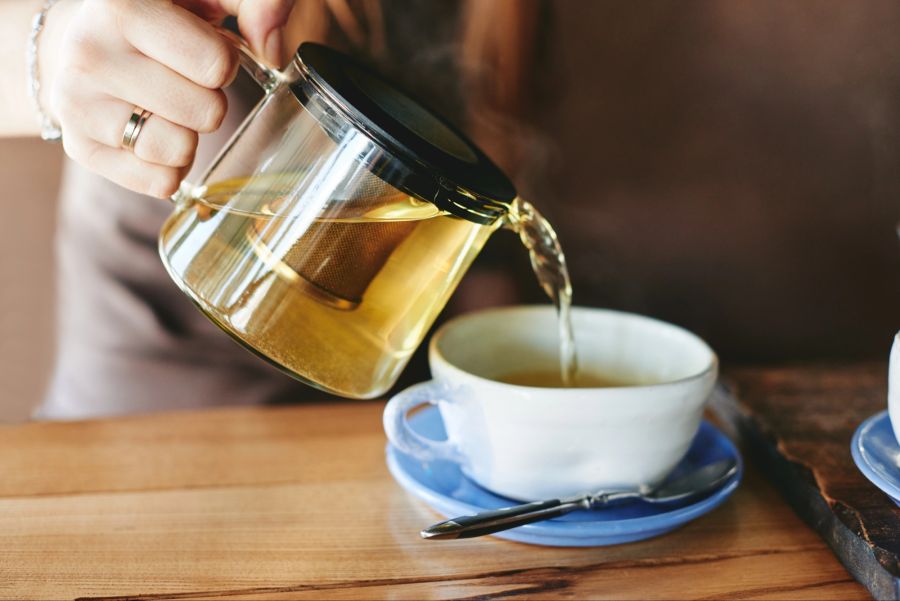 Person giesst grünen Tee in eine Tasse