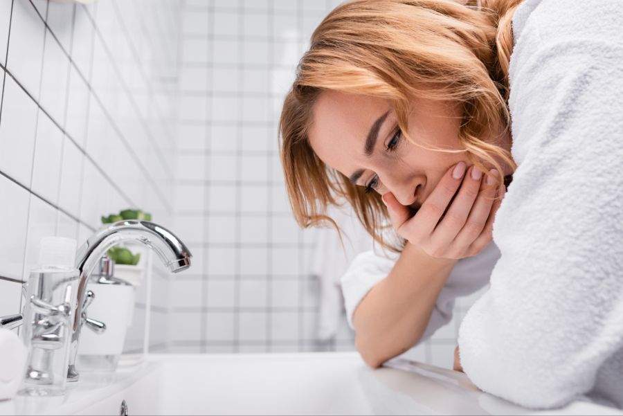 Frau mit Übelkeit vor einem Waschbecken