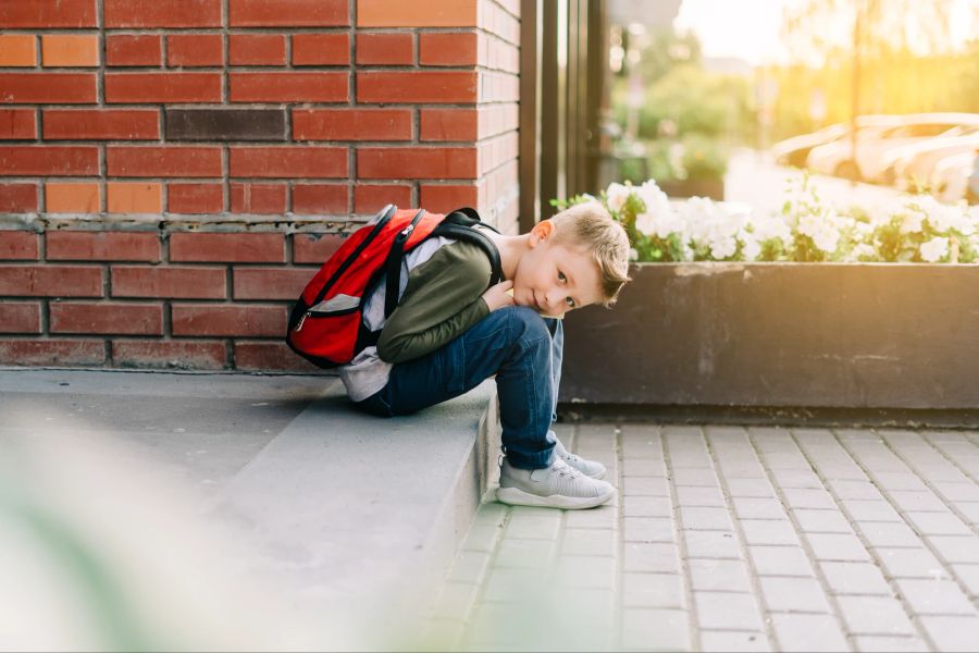 Kind mit Rucksack sitzt im Freien