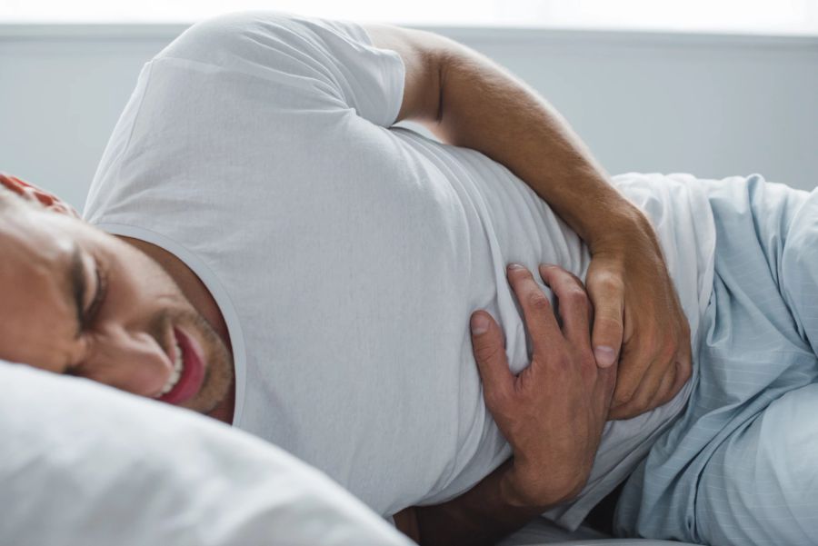 Mann liegt mit Bauchkrämpfen auf dem Bett.