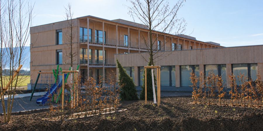 Modernes Holzgeb?ude mit Spielplatz und Pflanzbeeten
