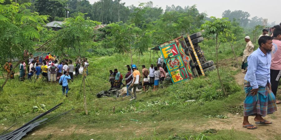 Menschen schauen zu, nachdem ein mit Eisenstangen und zusätzlichen Passagieren beladener Lastwagen auf einer Straße umgestürzt ist. Foto: Sohel Talukder/AP/dpa