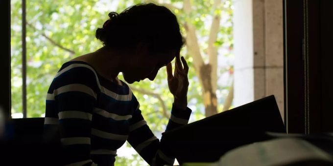 Anzeichen für einen Burn-out sind von aussen nicht immer leicht zu erkennen. Bestimmte Warnsignale können aber hellhörig machen. Frau sitzt über Buch im Dunkeln