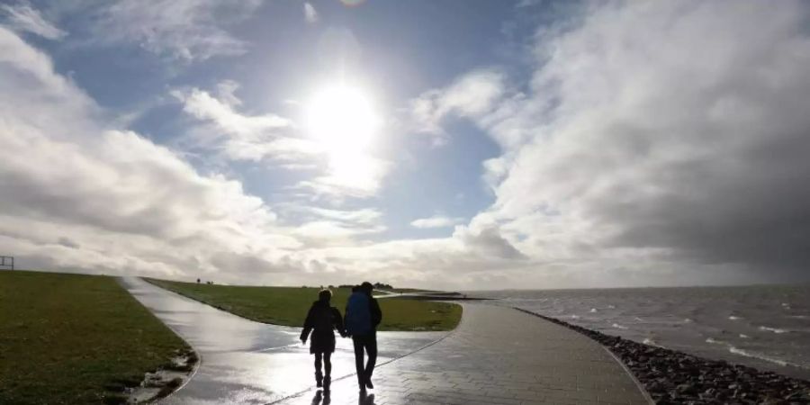 Spaziergänger sind bei Sonne am Deich in Dagebüll unterwegs. Foto: Bodo Marks/dpa