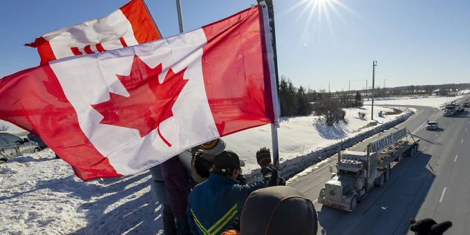 Unterstützer schwenken kanadische Fahnen auf einer Überführung vor vorbeifahrenden Lastwagen. Nach einer tagelangen Fahrt durch Kanada ist ein Konvoi aus Hunderten Lastwagen am Wochenende in der Hauptstadt Ottawa eingetroffen, um gegen Corona-Massnahmen und Impfvorschriften zu demonstrieren. Foto: Frank Gunn/The Canadian Press/AP/dpa Kanada Konvoi