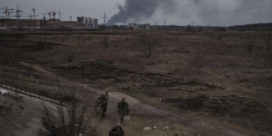 Soldaten gehen einen Weg entlang, während Rauch in Irpin nordwestlich von Kiew aufsteigt. Foto: Felipe Dana/AP/dpa