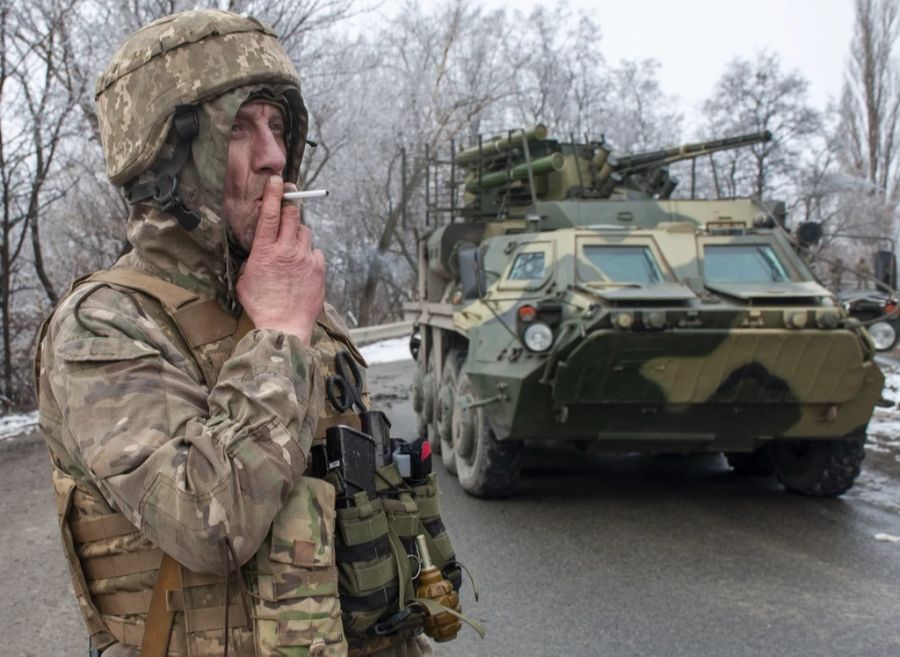 Ein ukrainischer Soldat raucht eine Zigarette vor seinem Panzer.