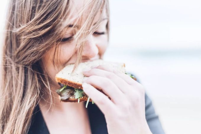 In einem Fertig-Sandwich stecken oft viele Konservierungsstoffe, Zucker und ungesunde Fette. Frau isst Sandwich
