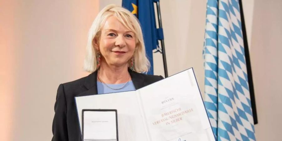 Rita Falk, Autorin, hält bei der Verleihung der Bayerischen Verfassungsmedaille im Landtag ihre Urkunde und Medaille in den Händen. Foto: Matthias Balk/dpa
