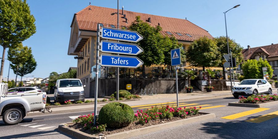 Ein Strassenwegweiser Richtung Schwarzsee, Fribourg und Tafers an der Hauptstrasse in Düdingen. Hinten der Gasthof zum Ochsen.