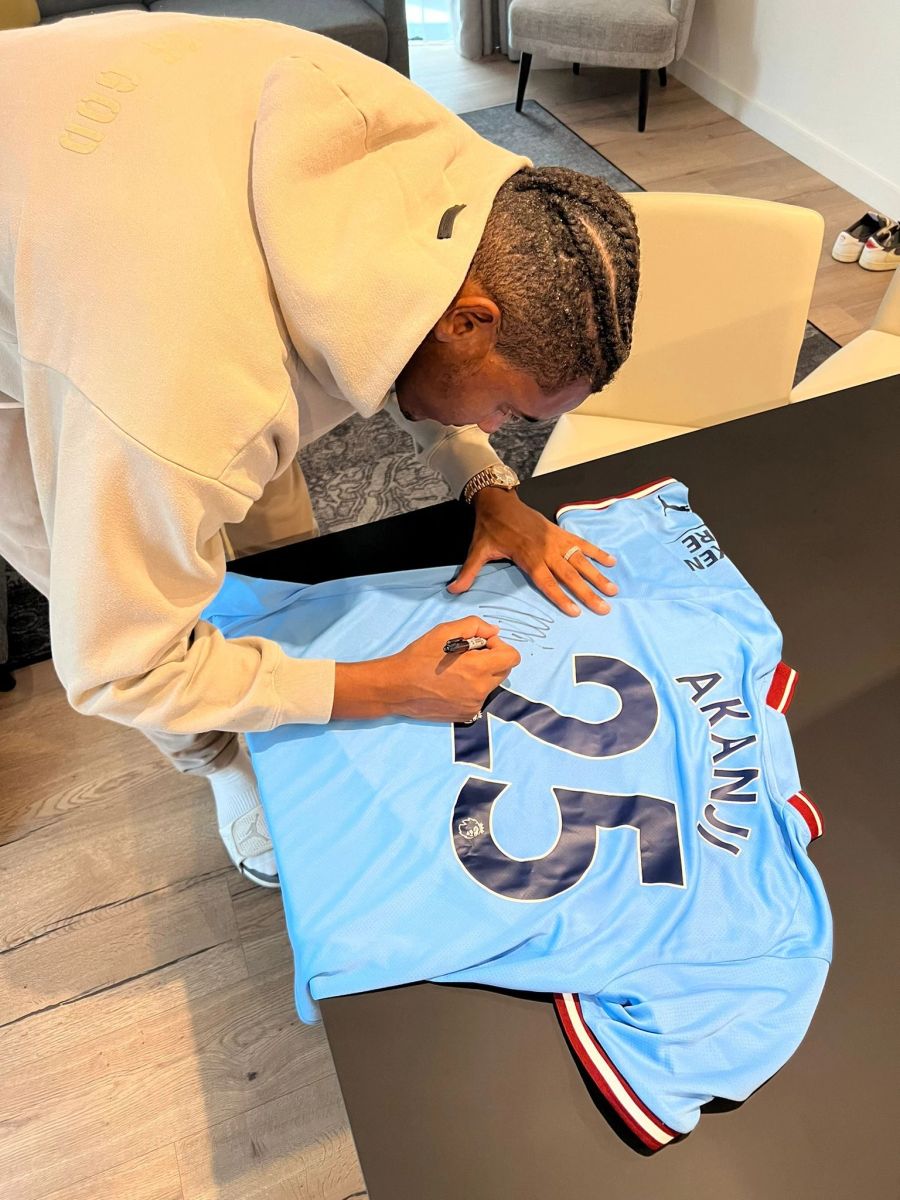 Manuel Akanji signiert ein Shirt seines neuen Clubs ManCity.