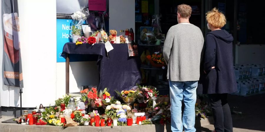 Menschen stehen vor der Tankstelle bei den für das Opfer gesammelten Blumen.