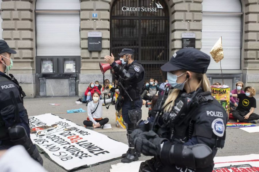 Ein Polizist steht vor der Blockade der Klimaaktivisten und spricht über ein Megafon.