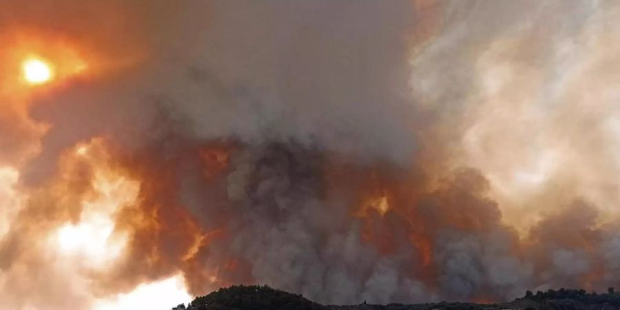 Rauch eines Waldbrandes steigt hinter einem Berghang in dem Ort Limni auf der Halbinsel Euböa etwa 160 Kilometer nördlich von Athen auf. Foto: Michael Pappas/AP/dpa