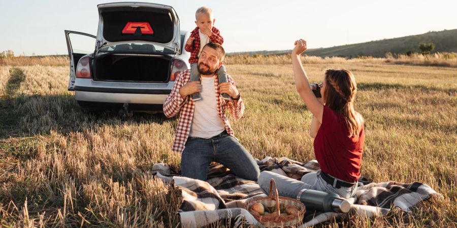 Familie mit Kleinkind macht Picknick im Freien, Auto auf dem Feld.