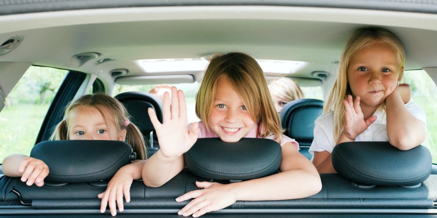 Drei Kinder sitzen auf der Rückbank eines Autos.