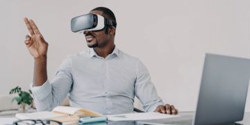Mann mit VR-Brille und Laptop am Schreibtisch
