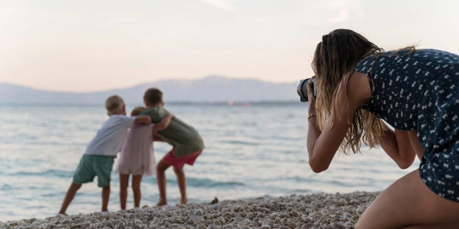 Frau fotografiert ihre Kinder am Strand.