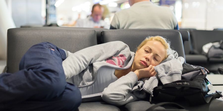 Frau schläft am Flughafen auf einer Sitzbank, mit Kopf auf dem Rucksack