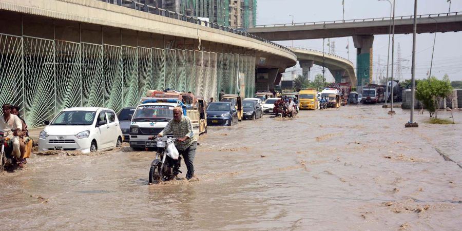 Motoradfahrer und Autos kämpfen sich durch eine überflutete Strasse in Karachi.