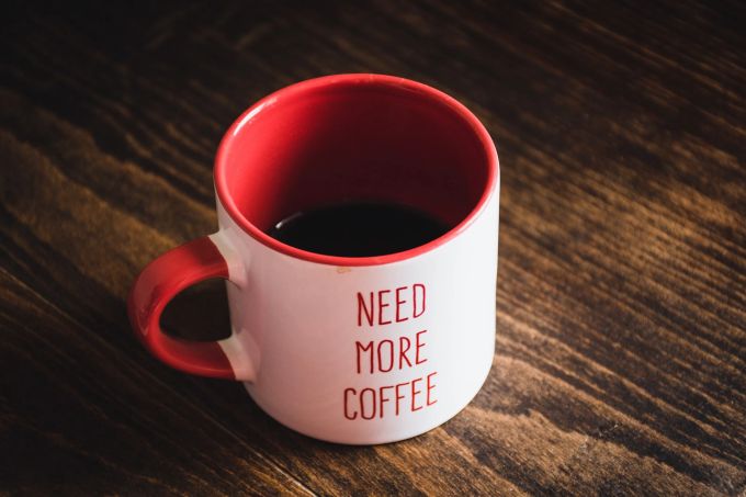 Koffein macht süchtig - schmeckt vor allem aber auch gut. Vor allem als Kaffee. Becher rot Kaffee Holztisch