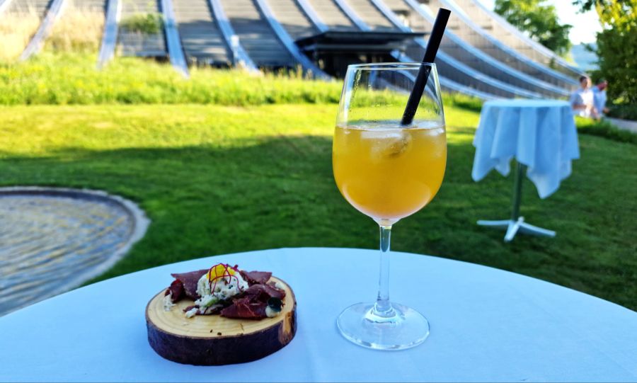 Bereits das Apéro-Holzplättli ist mit Hornochs-Patrami belegt. Dazu ein Schöngrün-Spritz bestehend aus Aprikose, Cava und Mineralwasser.