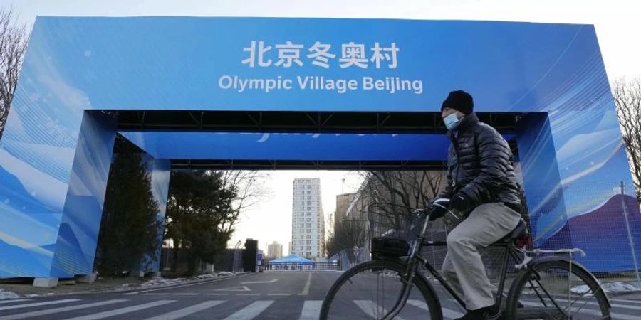 Ein Mann fährt in der Nähe des Athletendorfs in der chinesischen Hauptstadt Peking Fahrrad. Foto: -/Kyodo/dpa