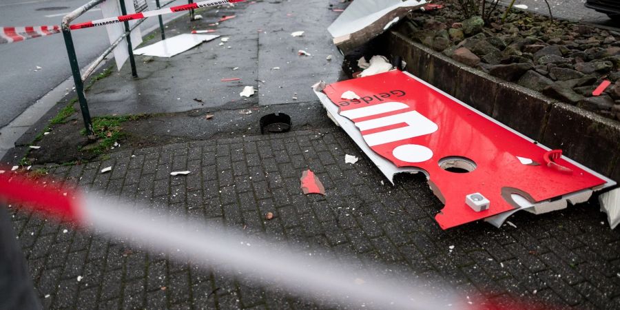 Ein zerstörtes Schild mit dem Logo der Sparkasse liegt auf dem Boden nahe eines gesprengten Geldautomaten.