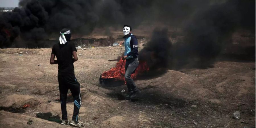 Ein Palästinenser mit einer Guy Fawkes-Maske zieht bei Protesten an der Grenze zu Israel im Gazastreifen einen brennenden Reifen.