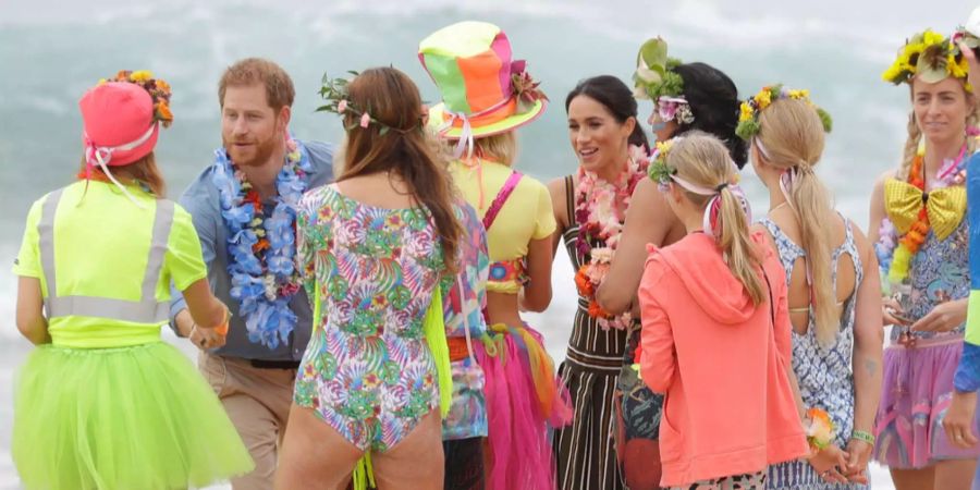 Prinz Harry und seine Frau Meghan sprechen am berühmten Bondi Beach in Sydney mit Blumenketten tragenden Surfern.