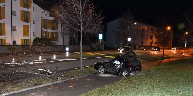Ein völlig demoliertes Auto steht auf einem Trottoir neben einer Hauptstrasse.