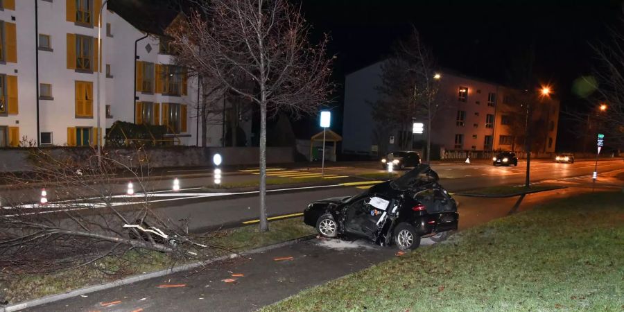 Ein völlig demoliertes Auto steht auf einem Trottoir neben einer Hauptstrasse.