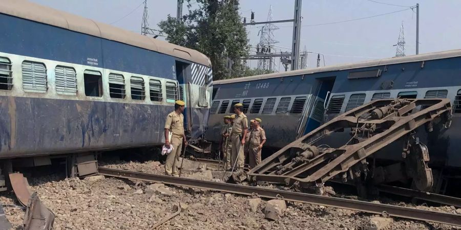 Indische Sicherheitskräfte stehen vor den Waggons eines entgleisten Zuges in Raebareli (IND), die sich ineinander verkeilt haben.