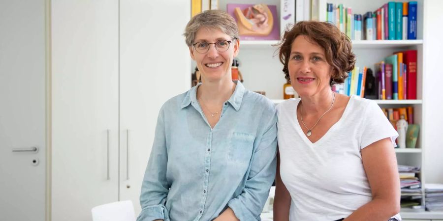 Natascha Nicklaus (l) und Nora Szász, Frauenärztinnen, lehnen in ihrer Praxis an einem Tisch.