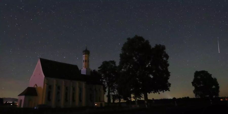 Ein Meteor verglüht am Himmel über der Wallfahrtskirche Sankt Coloman (D).