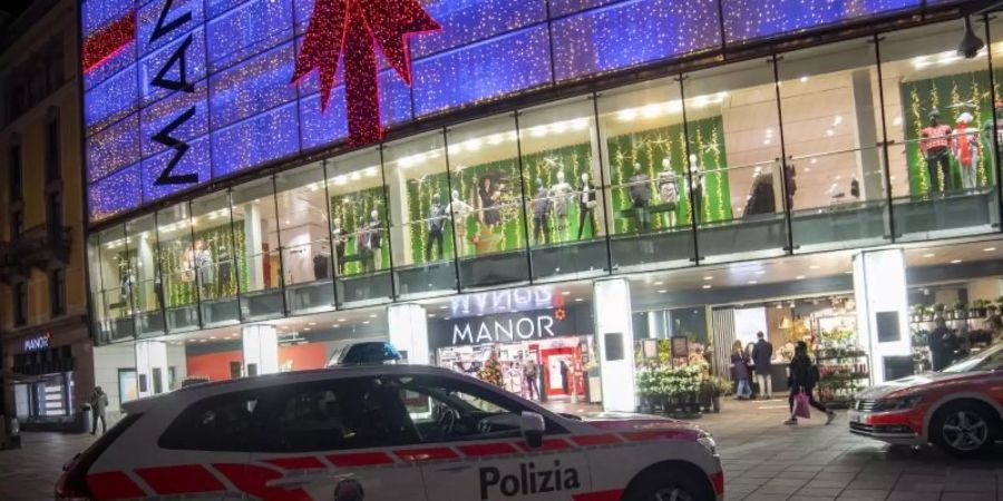 Polizeifahrzeuge stehen vor dem Kaufhaus Manor an der Piazza Dante im schweizerischen Kanton Tessin. Eine Frau hat in dem Warenhaus heute zwei Passantinnen mit einem Messer angegriffen. Foto: Pablo Gianinazzi/KEYSTONE/Ti-Press/dpa