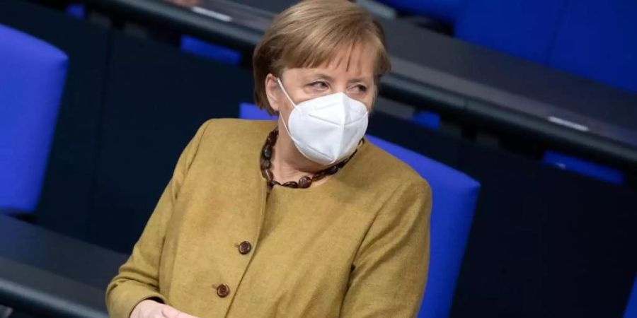 Bundeskanzlerin Angela Merkel (CDU) steht zu Beginn einer Plenarsitzung im Bundestag mit Schutzmaske an ihrem Platz. Foto: Bernd von Jutrczenka/dpa