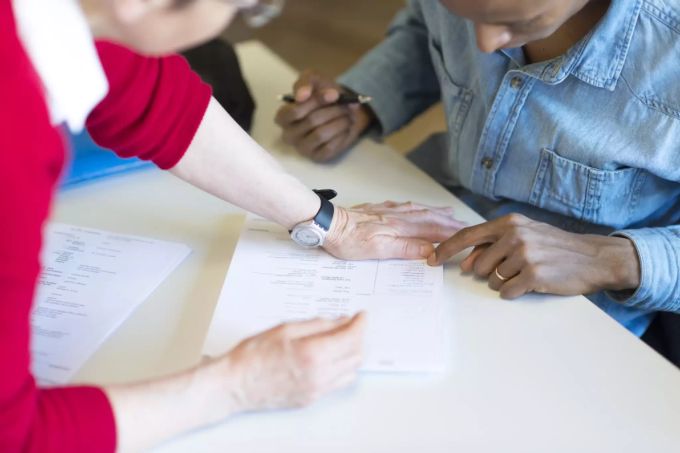 Eine Frau hilft einem Mann mit Migrationshintergrund bei einem Formular. coronavirus